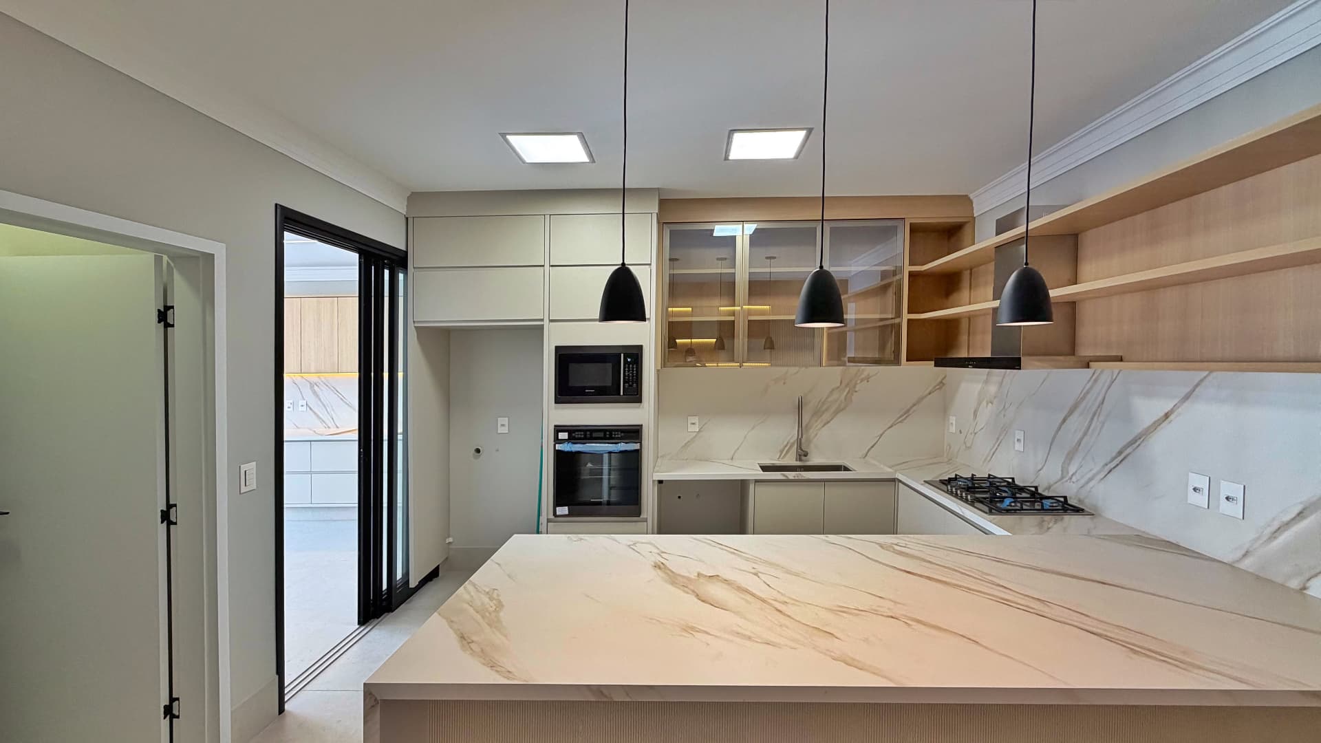 Cozinha com ilha em porcelanato marmorizado e pendentes pretos