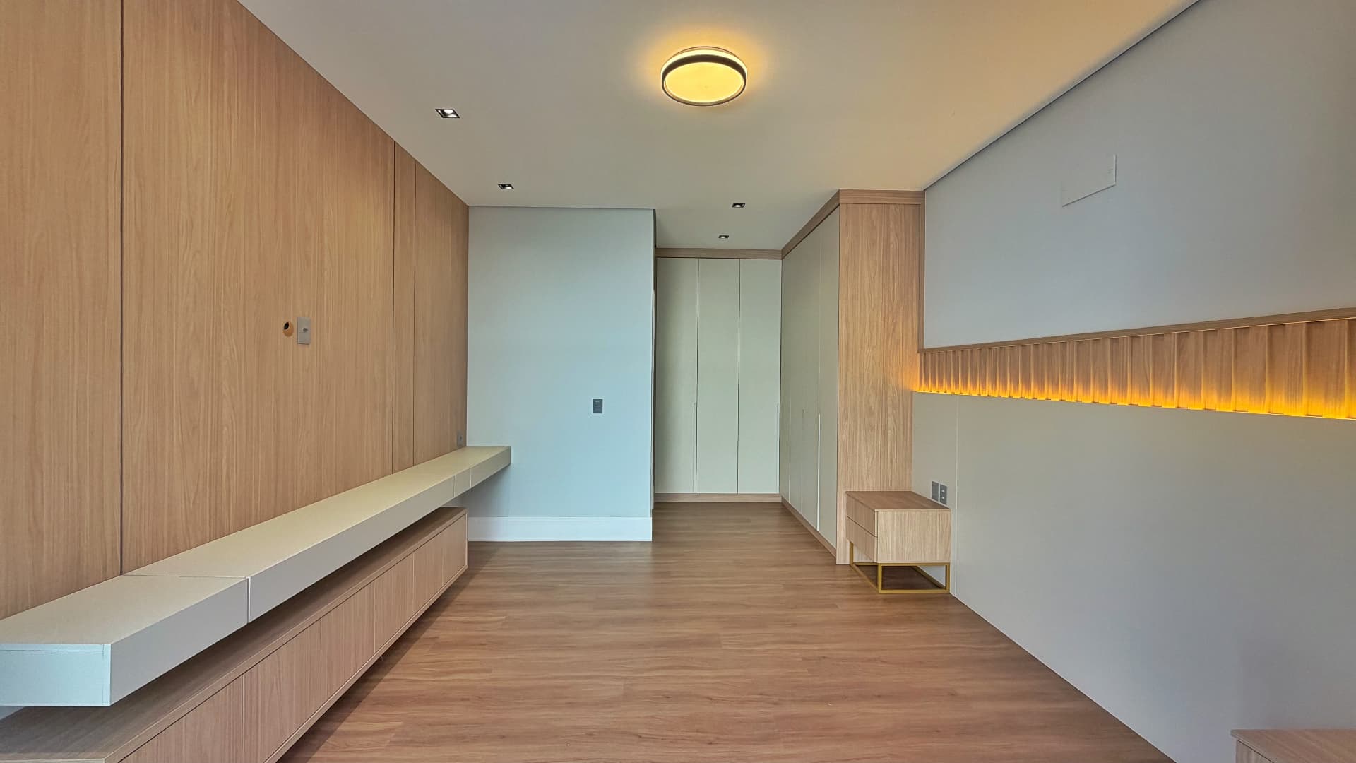 Suíte com painel de madeira, bancada e closet ao fundo