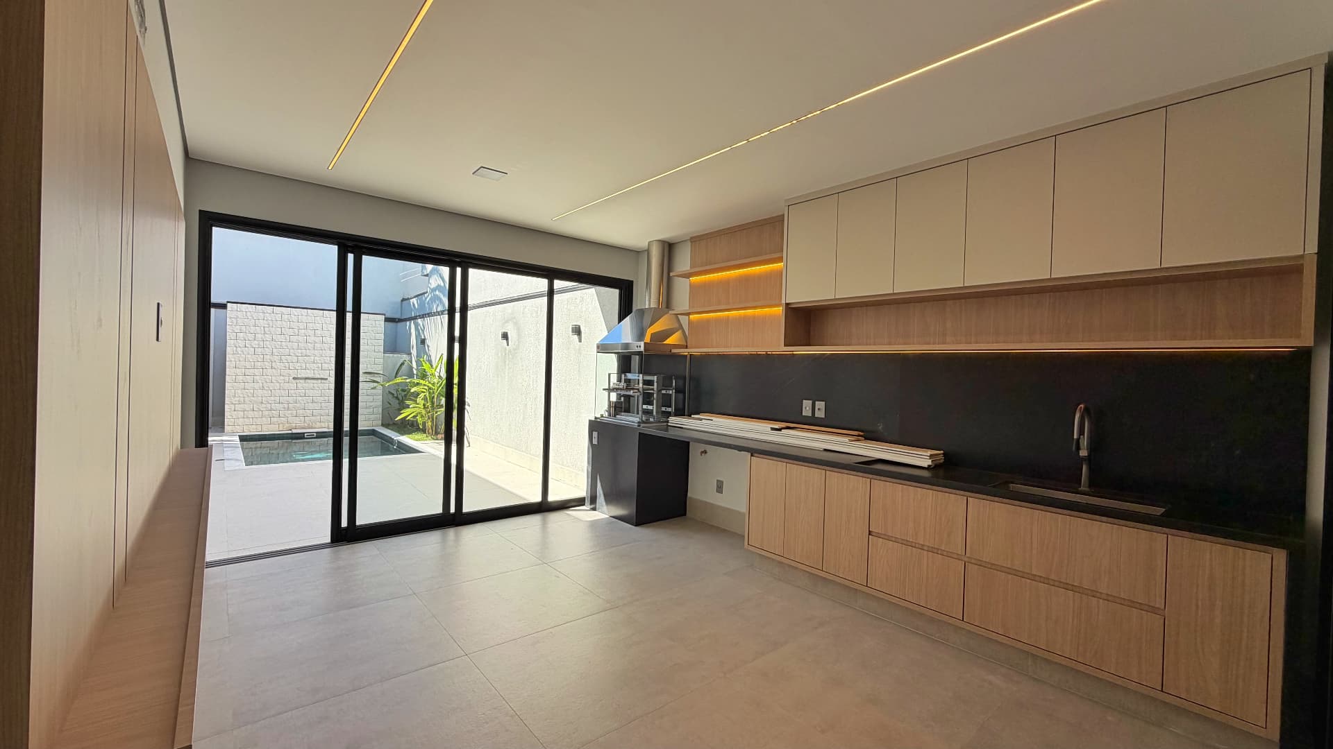 Área gourmet com churrasqueira, bancada preta e vista para a piscina