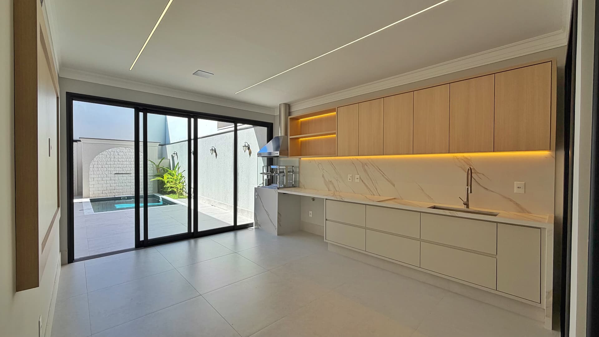 Área gourmet com bancada iluminada e porta de vidro para a piscina