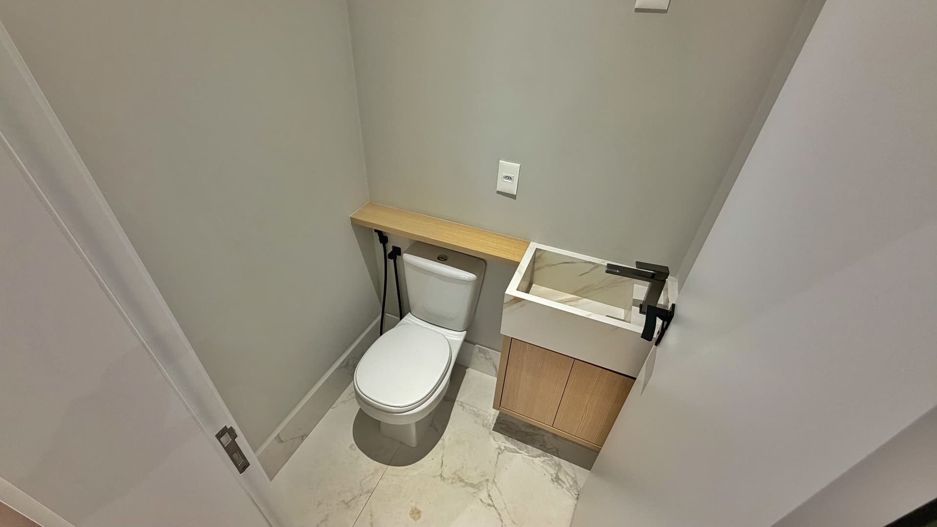 Lavabo com cuba esculpida, marcenaria em madeira clara e piso marmorizado