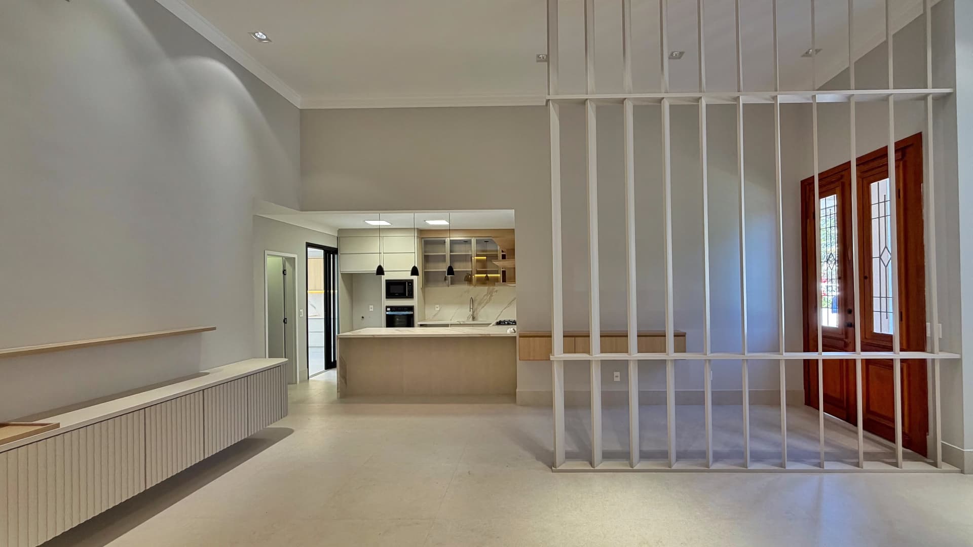 Living com pé-direito alto, aparador ripado e vista para a cozinha