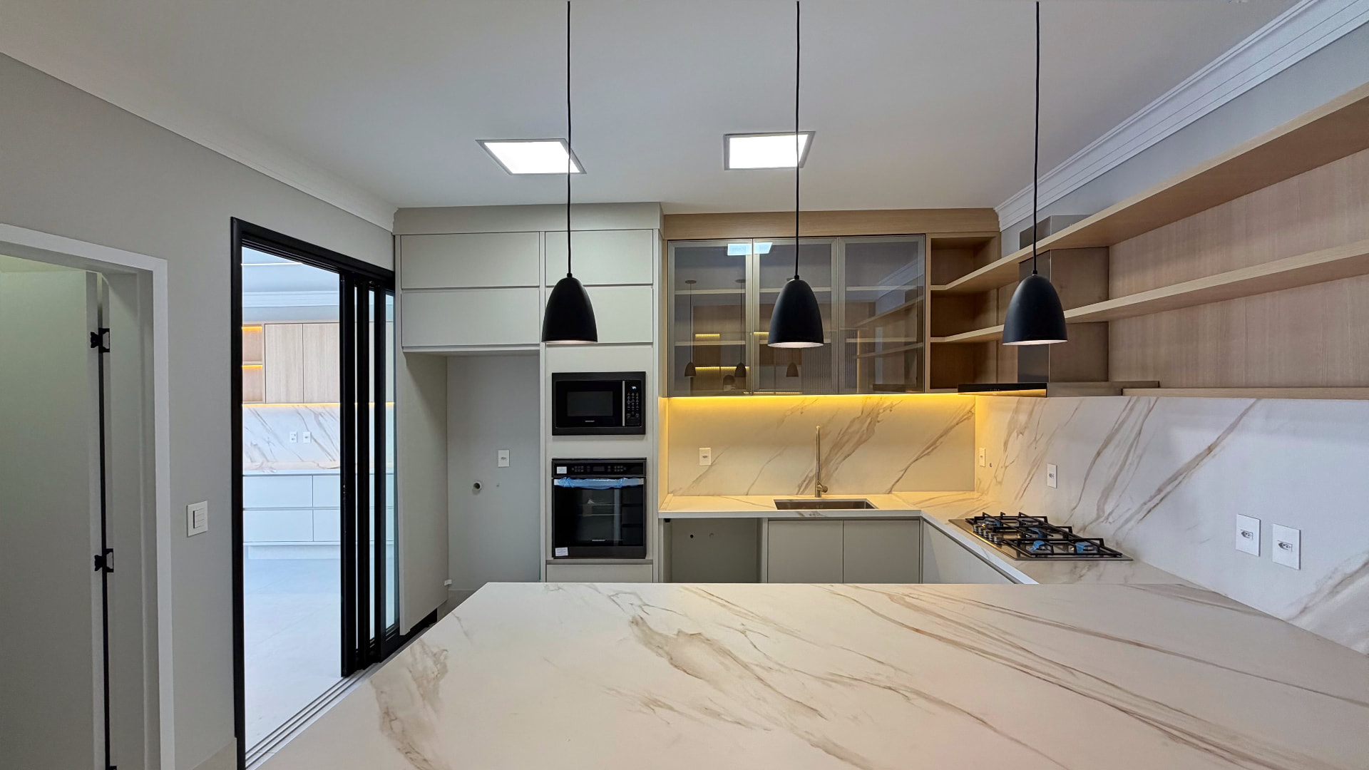 Cozinha com ilha em porcelanato marmorizado, pendentes pretos e forno embutido