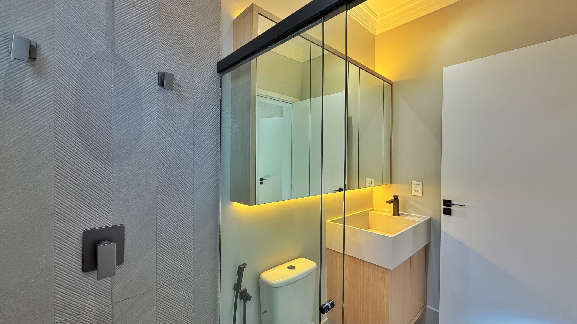 Banheiro com espelheira iluminada, box amplo e revestimento texturizado