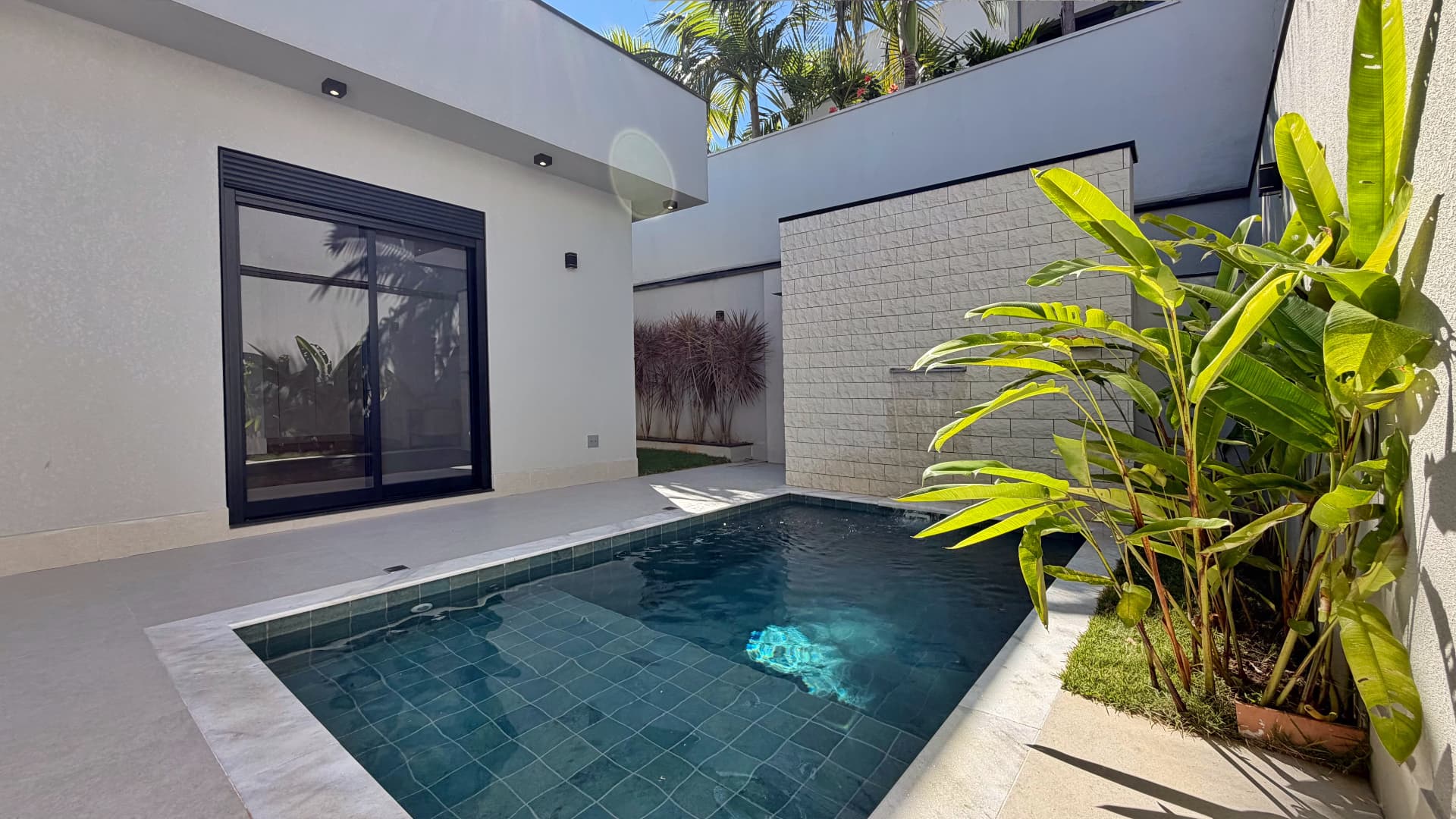 Piscina com deck, revestimento em pedra e paisagismo tropical