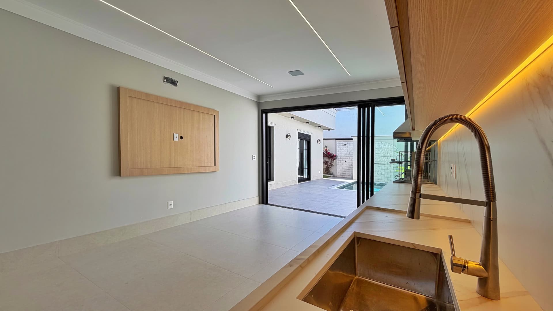 Espaço gourmet com painel de TV em madeira e vista para a piscina