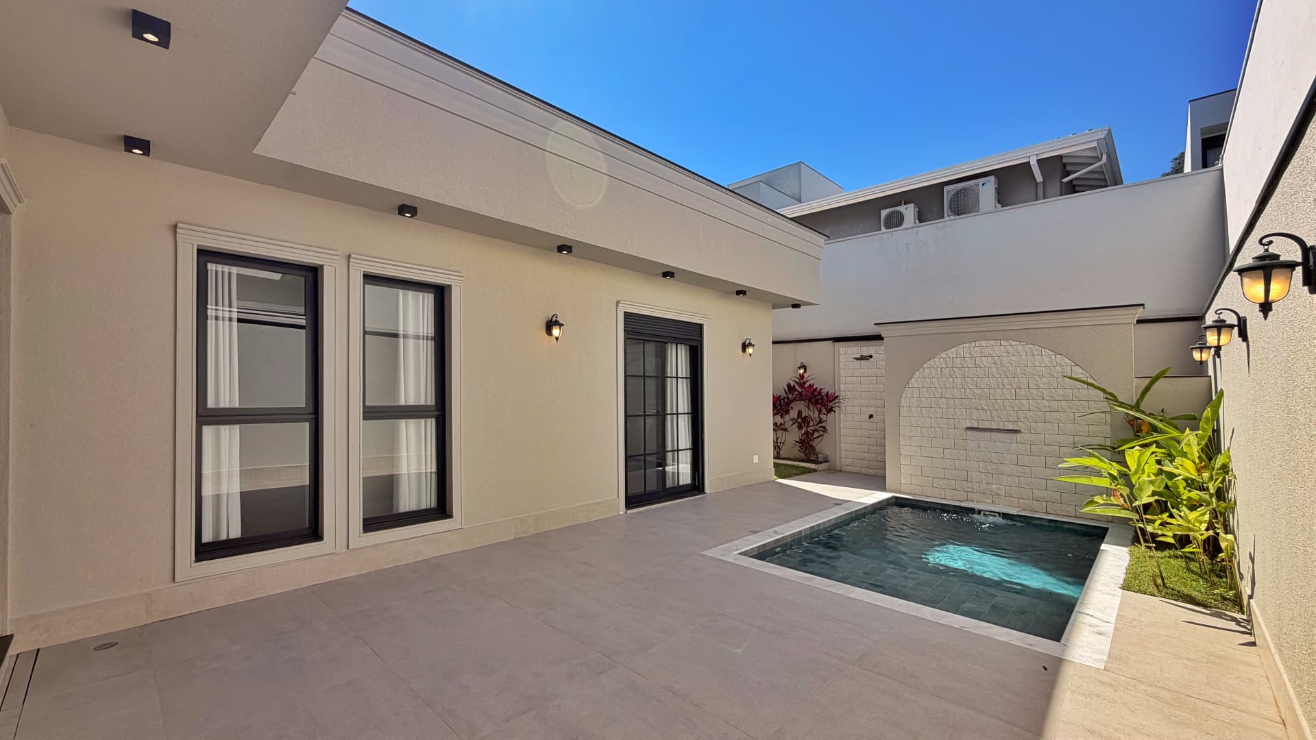Área de lazer com piscina, deck em porcelanato e janelas amplas