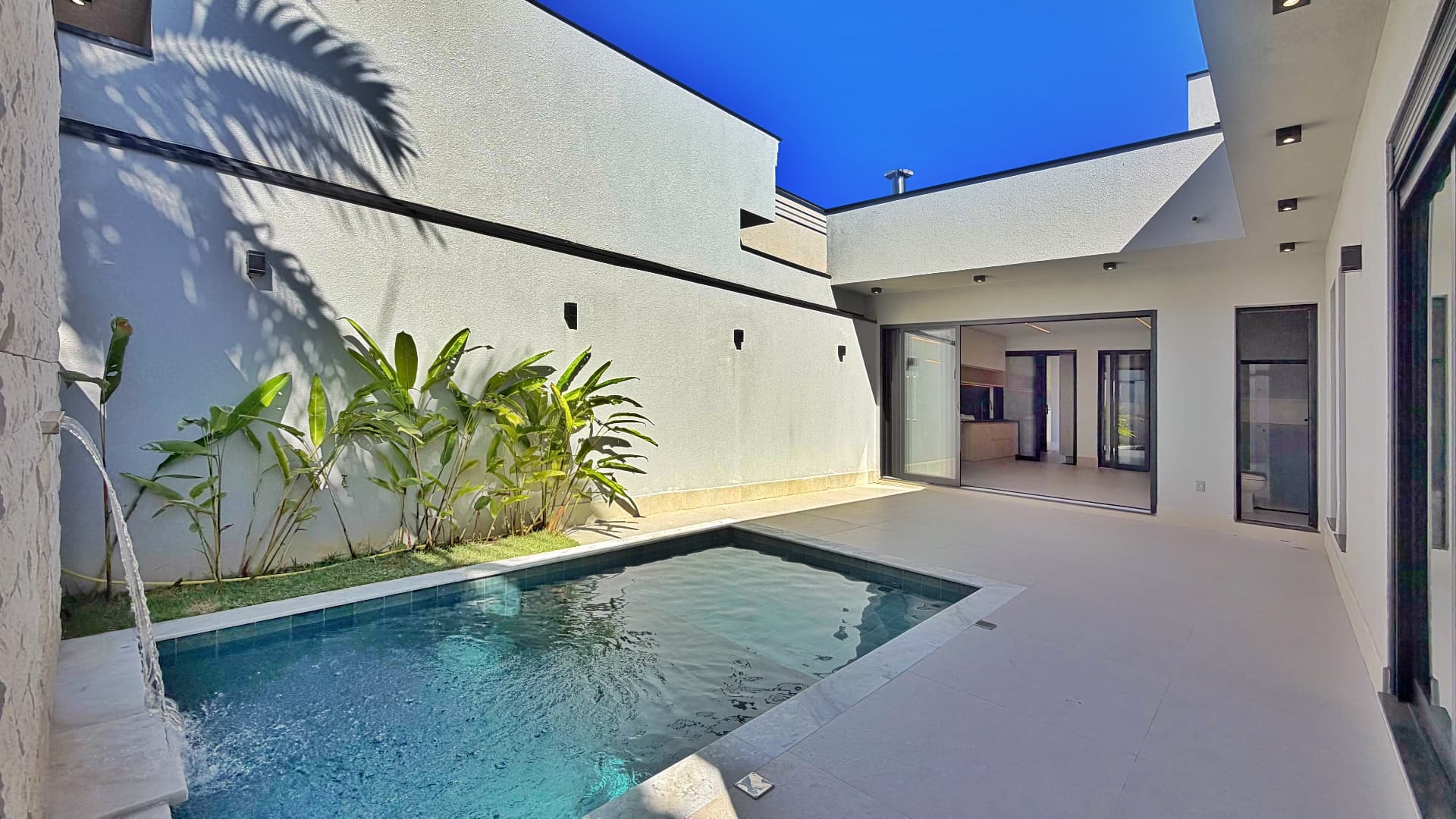 Piscina com cascata, plantas tropicais e integração com a área interna