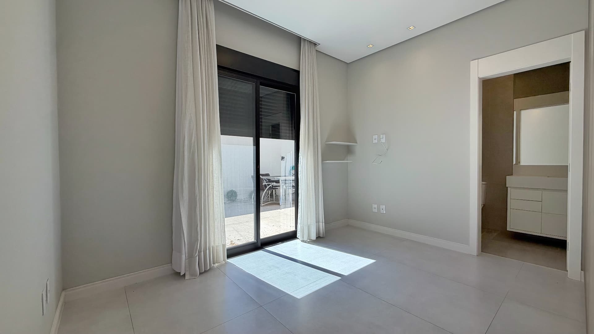 Suíte com cortinas, porta de vidro para o quintal e banheiro anexo